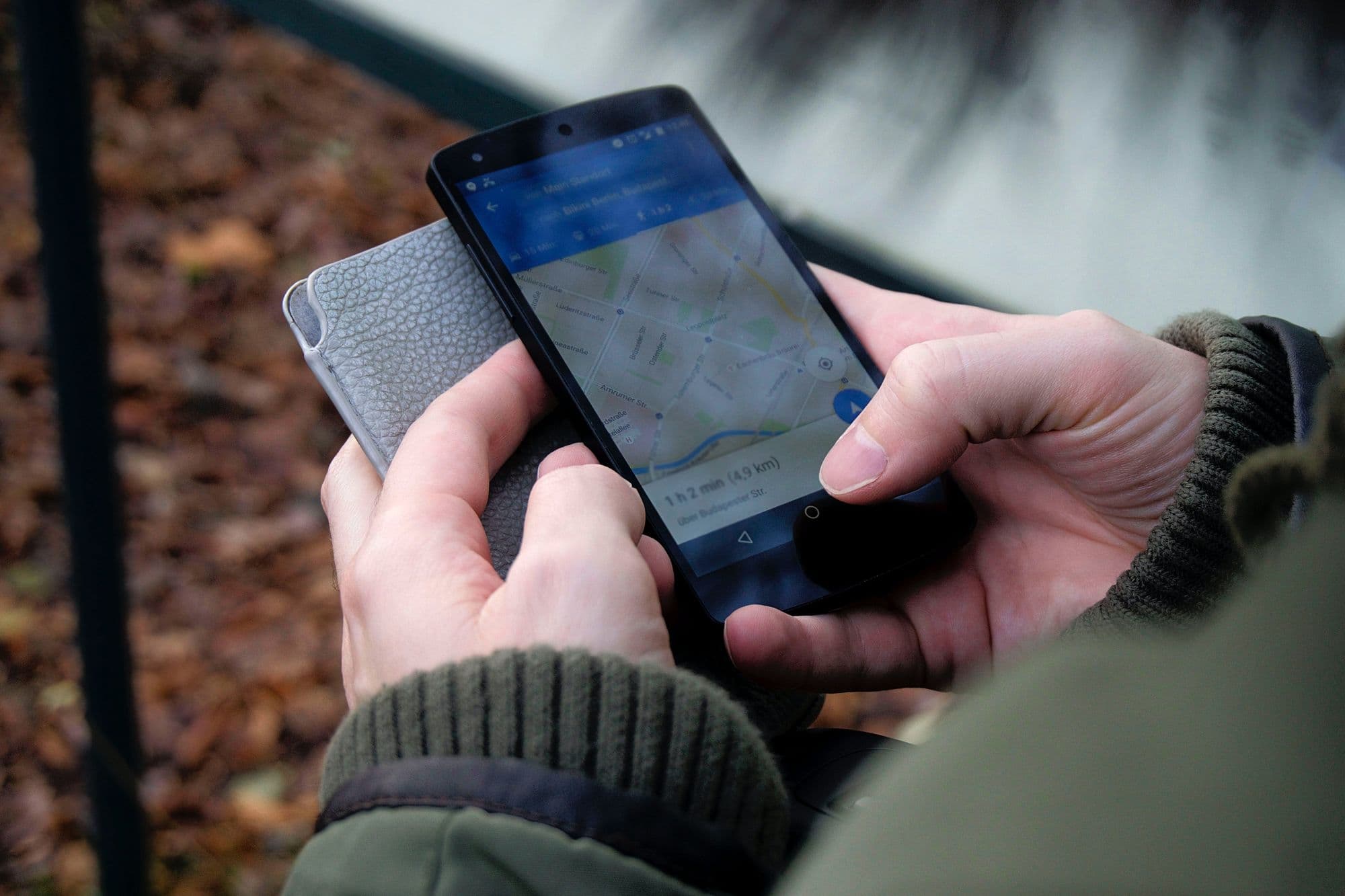 Hands holding an Android phone with a map open, autumn leaves behind