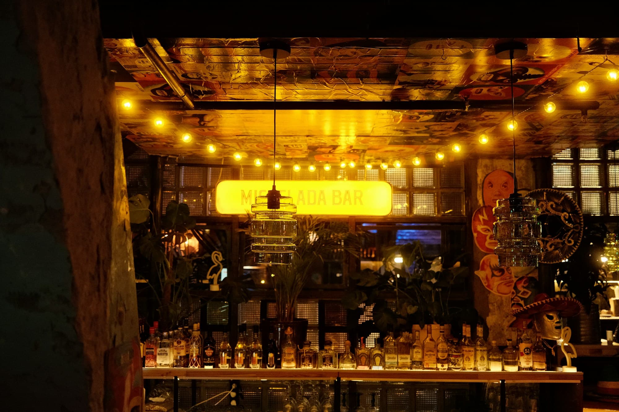 A bar interior lit warmly at night with string lights and a bottle display