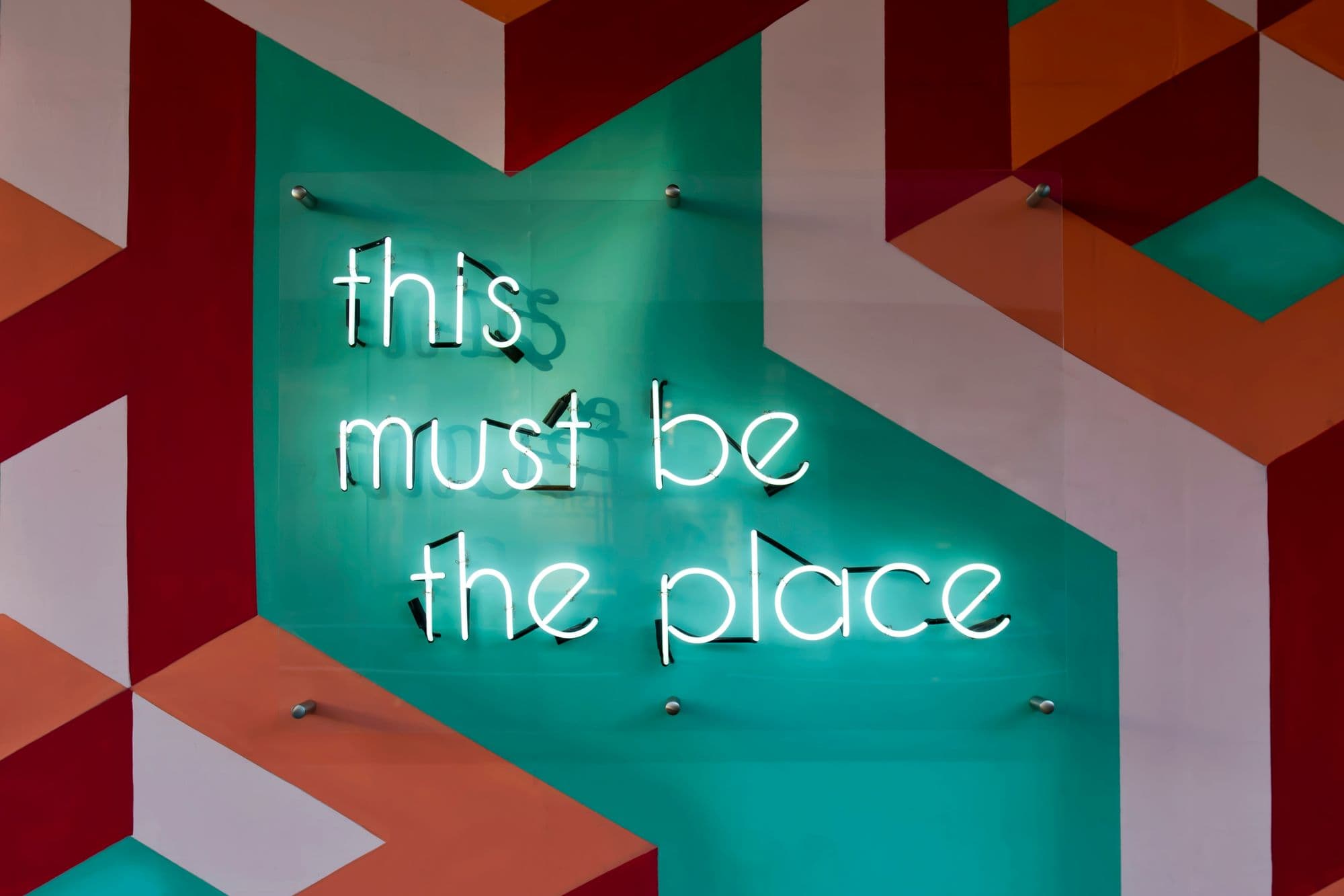 A neon sign reading this must be the place on a painted geometric wall