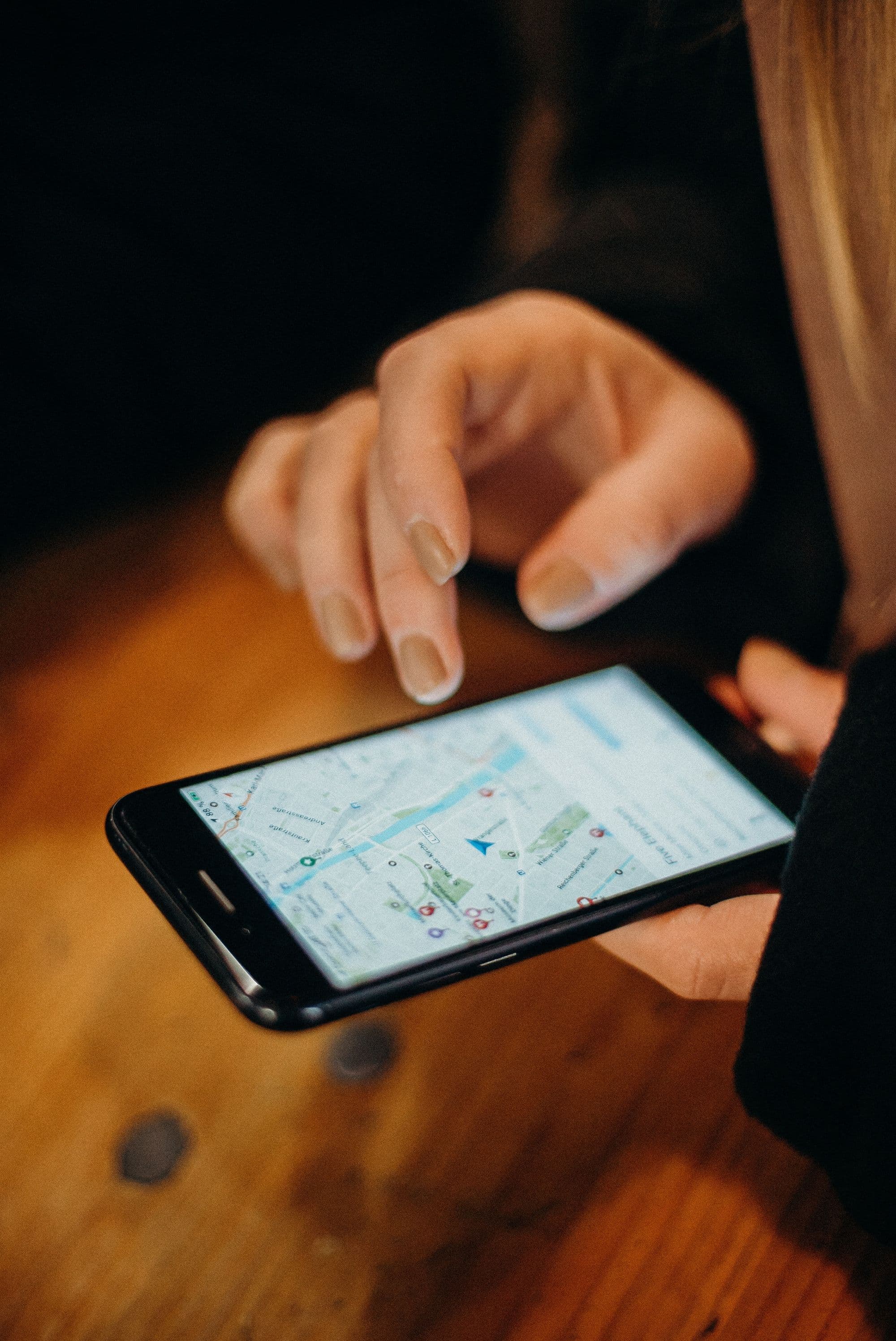 Two hands holding a smartphone with a street map open over a wooden table