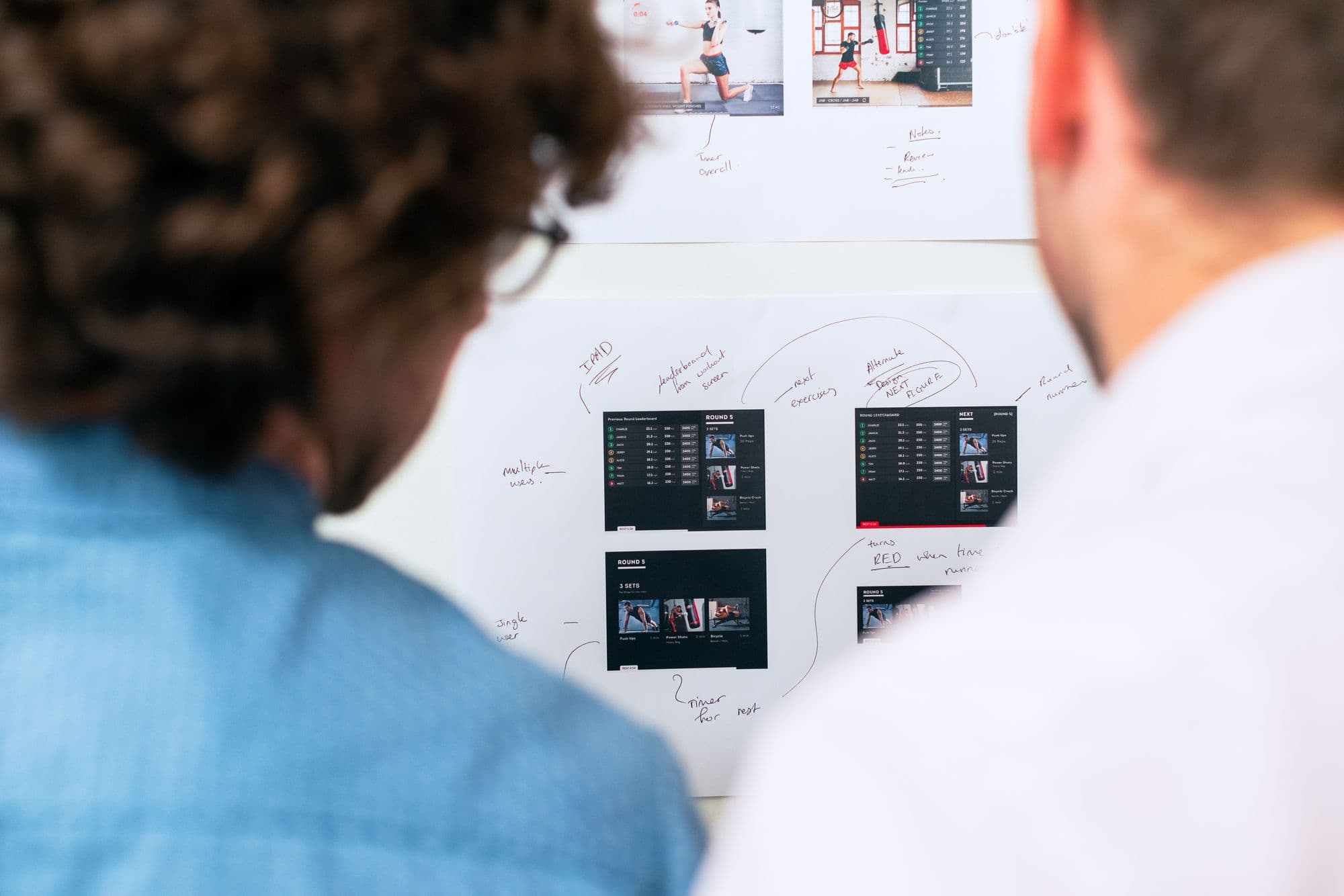 Two people reviewing website design printouts pinned to a wall