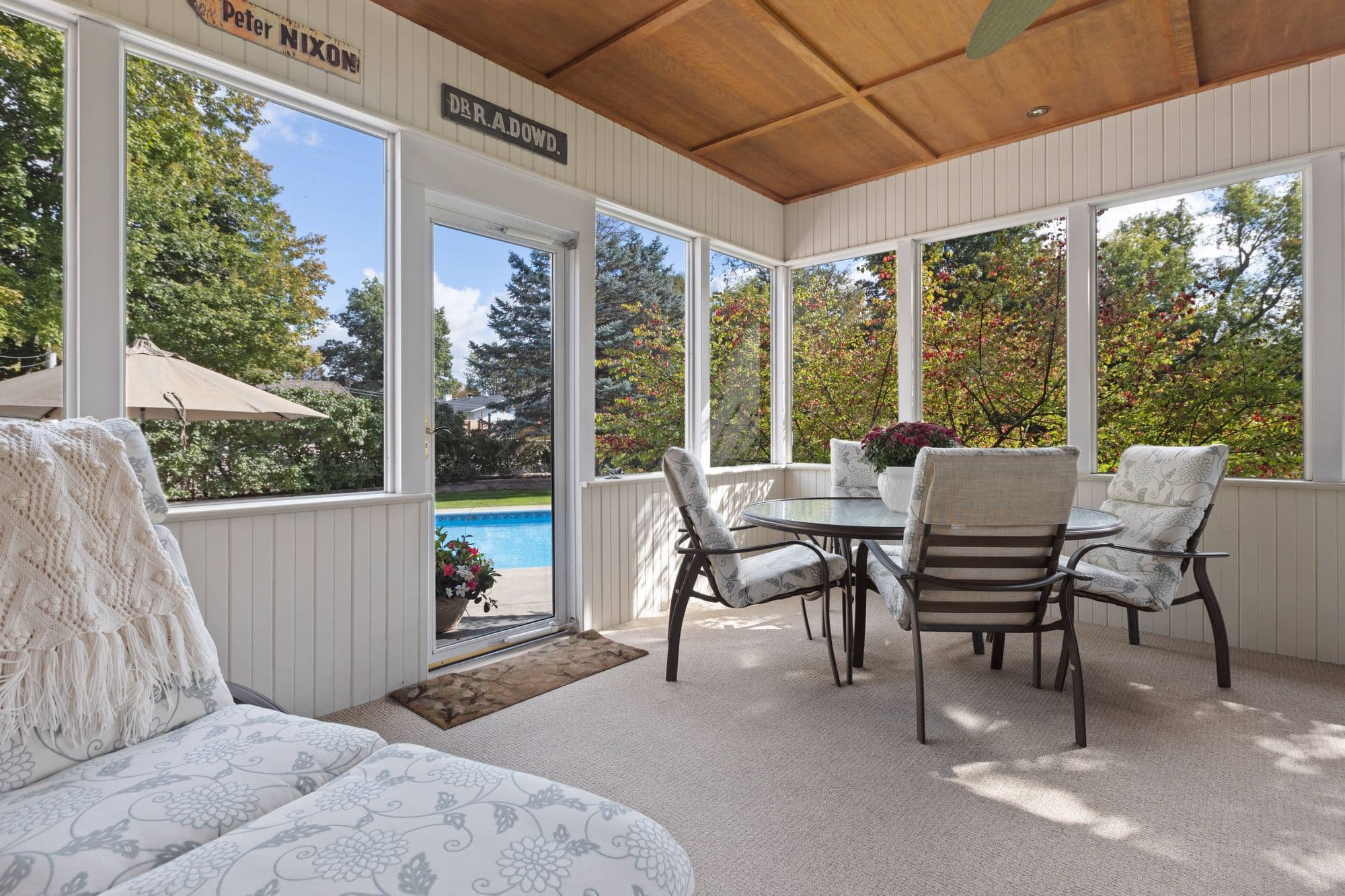 A bright screened sun porch with a dining table and a pool beyond the windows